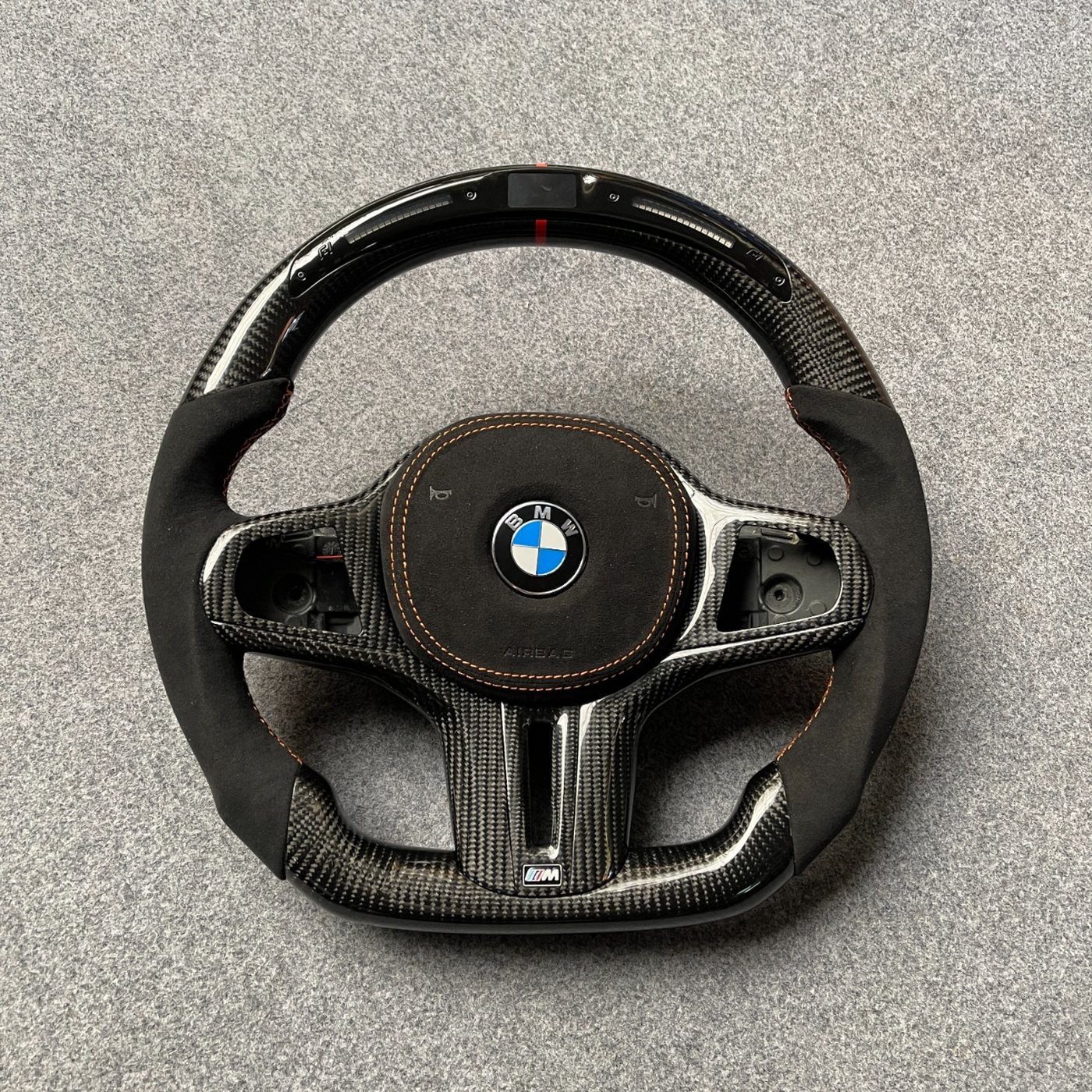 BMW G series custom carbon fiber steering wheel with black Alcantara, LED display, red centerline and orange stitching by Miami Carbon Designs
