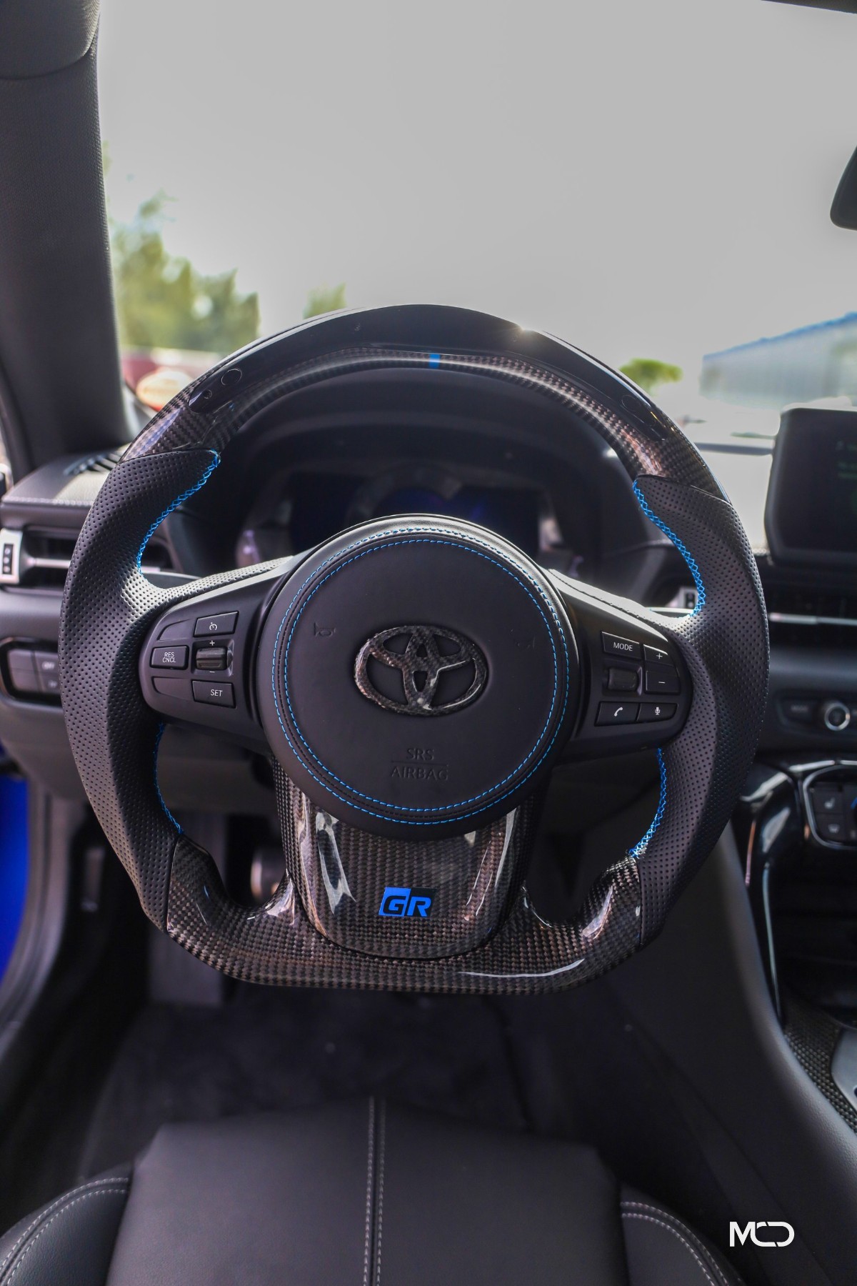 Toyota GR Supra custom carbon fiber steering wheel installed, black perforated leather, blue stitching, leather airbag cover, gloss carbon