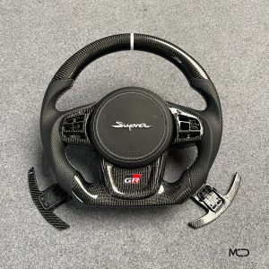 Toyota GR Supra custom carbon fiber steering wheel, black perforated leather, white stitching, white stripe, custom airbag cover with Supra logo, carbon paddle shifters